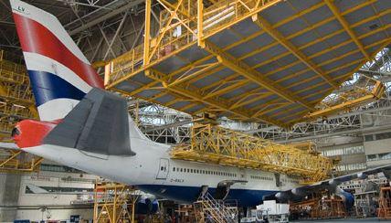 Large British Airways plane inside a warehouse with scaffolding and workers around it.