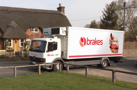A Brakes lorry parked outside a home with a thatched roof.