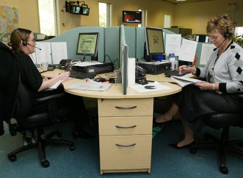 Wooden desk with two Crimestoppers employees wearing headphones and working on their computers.