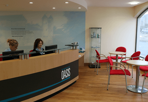 Oasis reception desk with two women working behind it, tables and chairs are set out to the right of the desk.