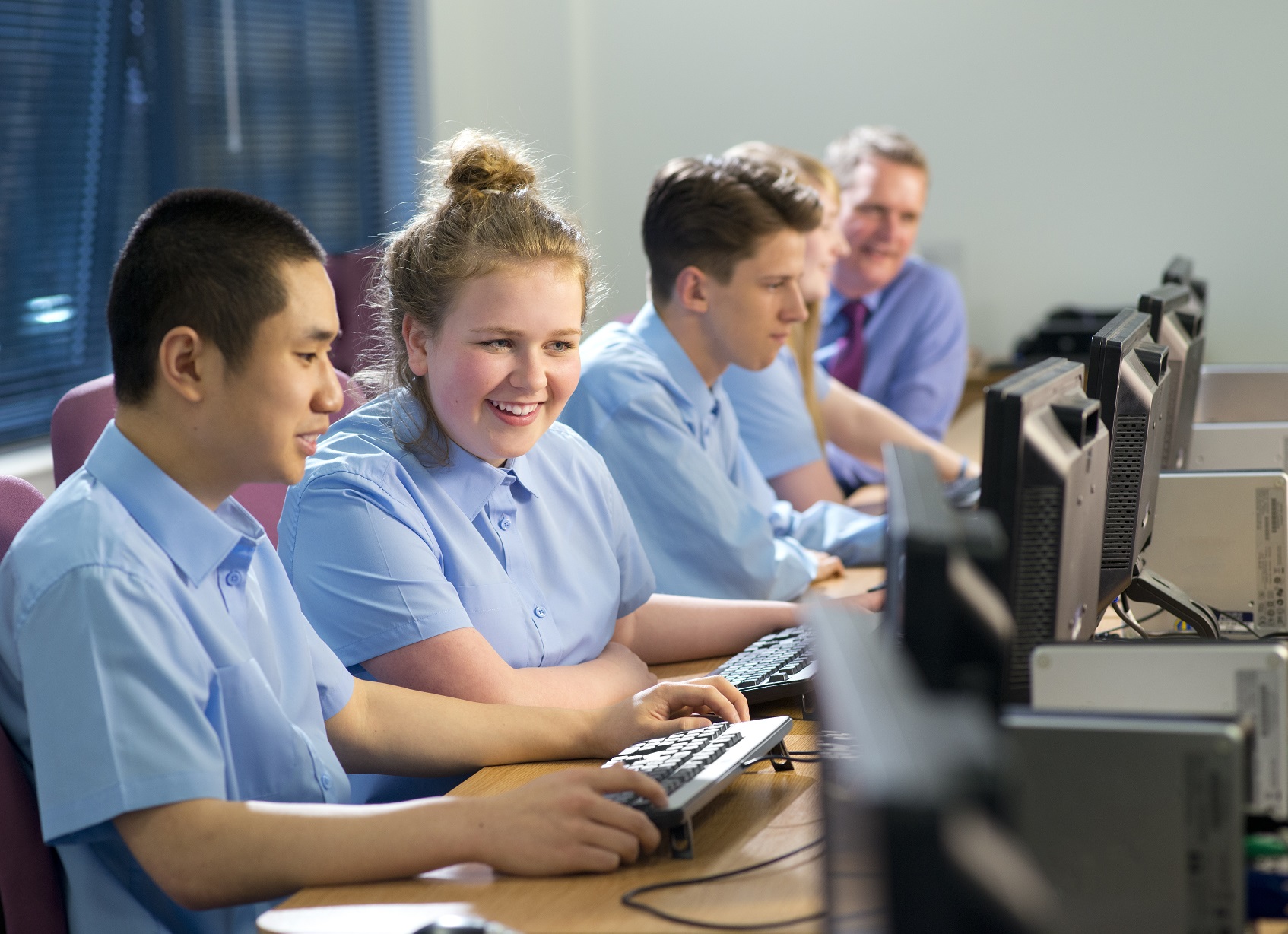 School kids at computers, boy and girl in foreground are laughing together.