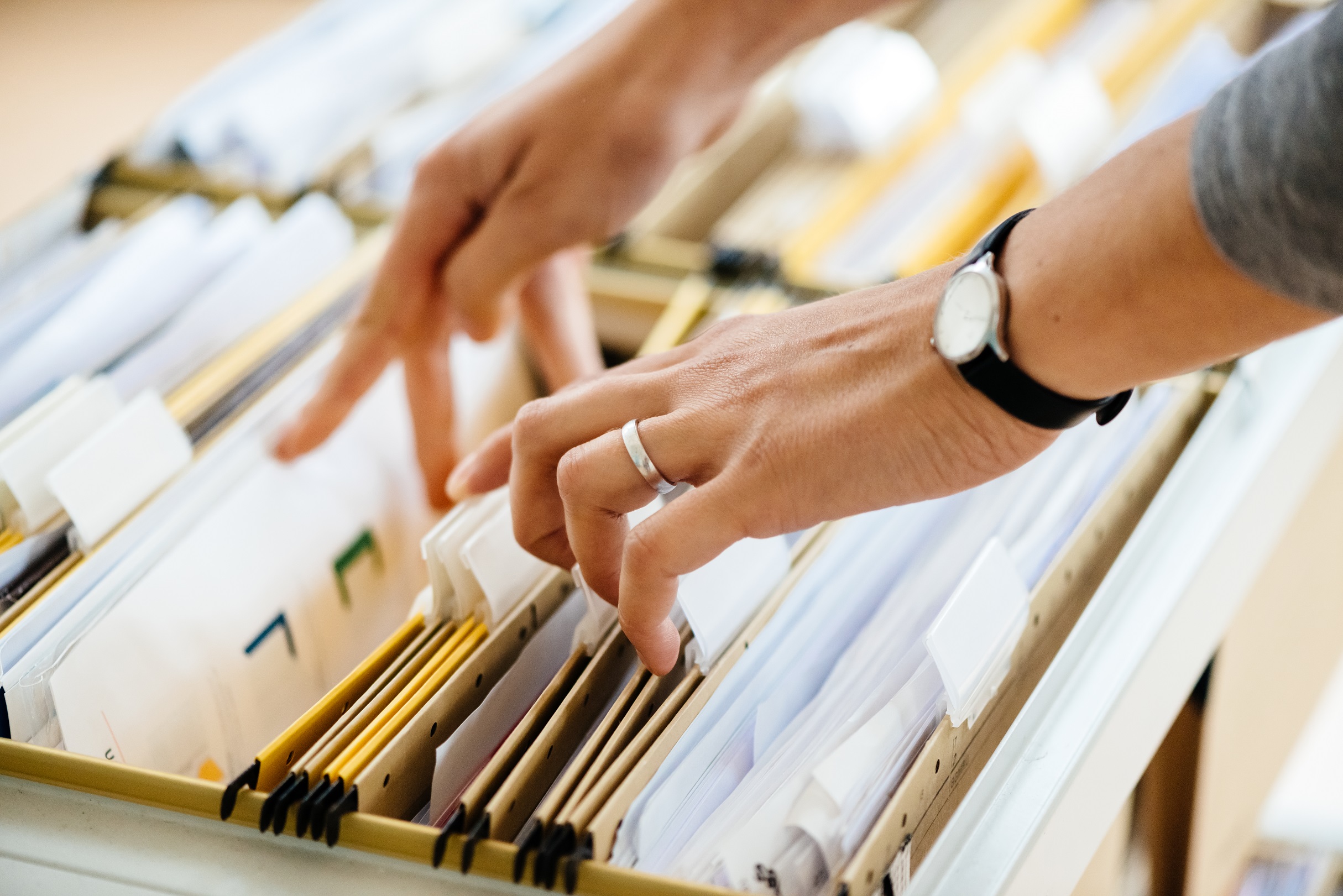 Hands searching through files in an open cabinet drawer.