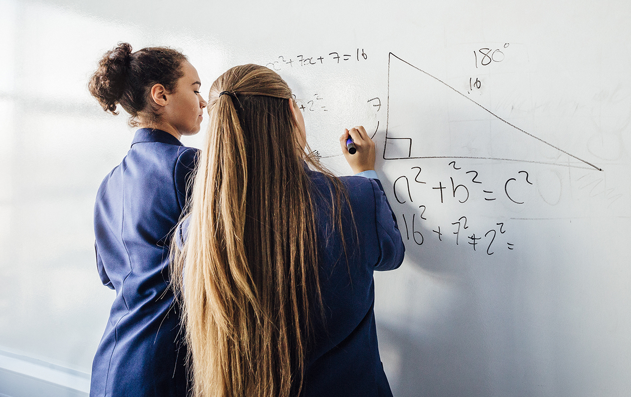 Two school girls solving a maths problem on a white board.