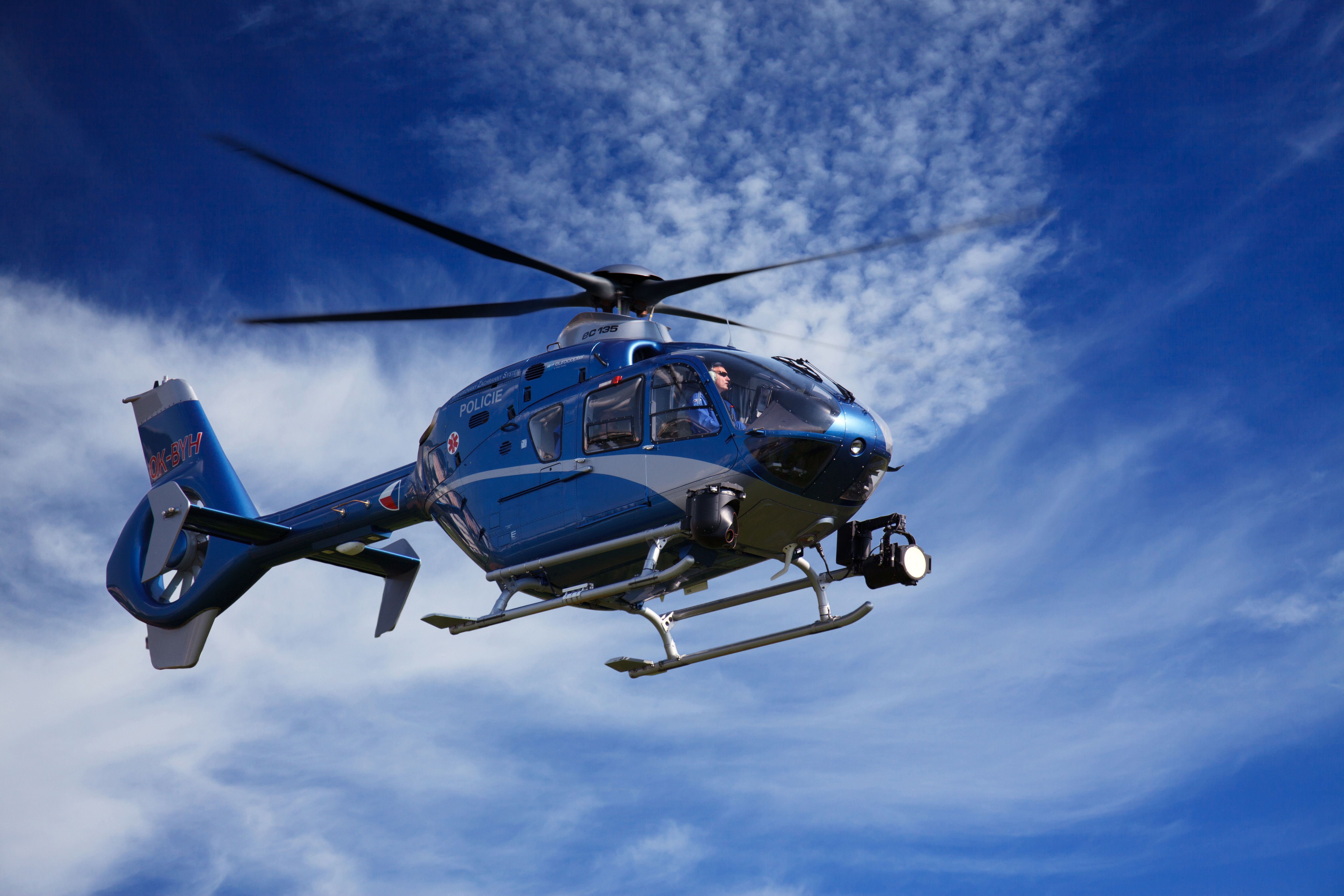 Blue Police helicopter flying in front of blue skies with a little cloud.