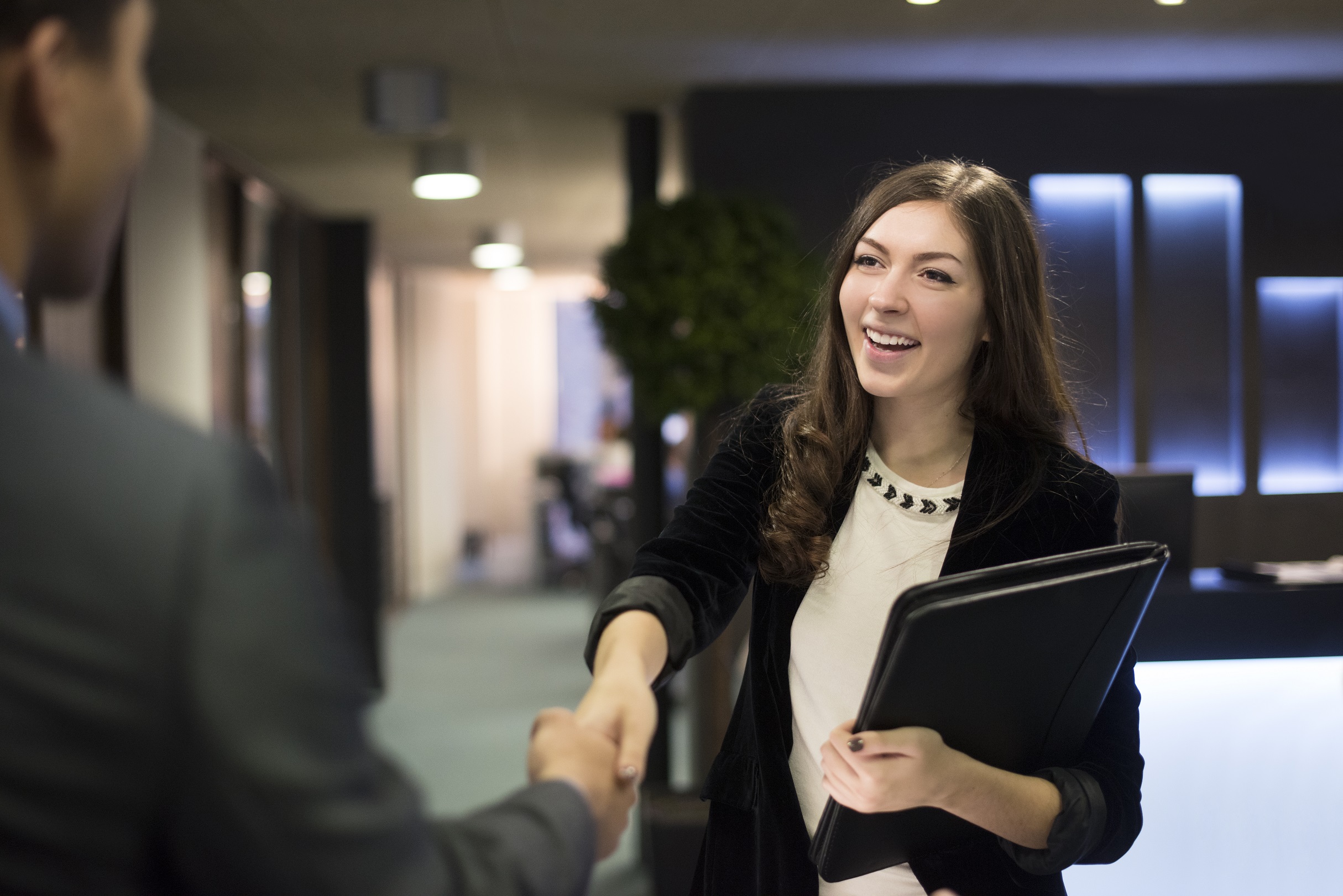 Businesswoman in black suit shaking hands with a business man in a grey suit.