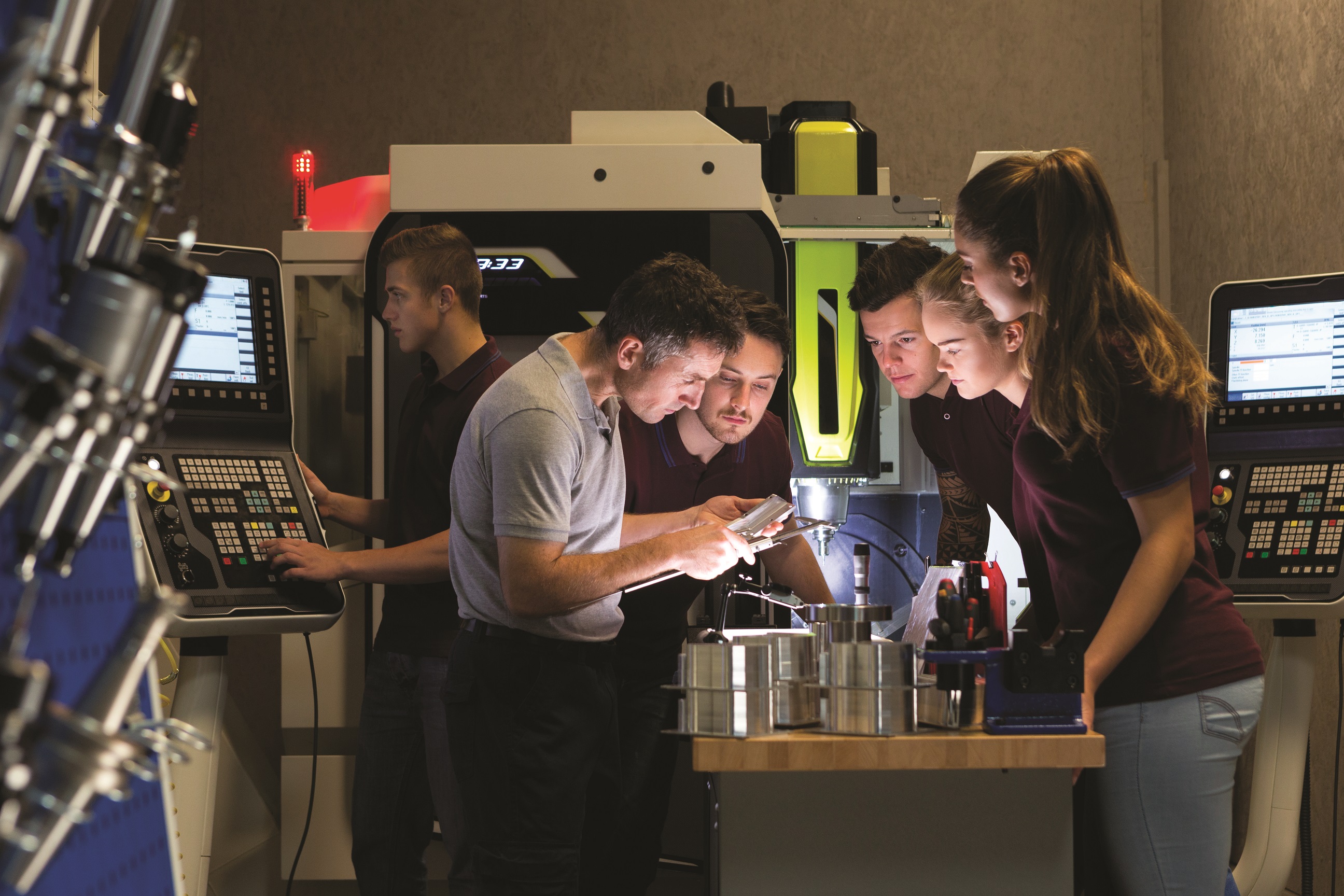 A team of workers in a robotics lab are gathered around a table and are deep in thought